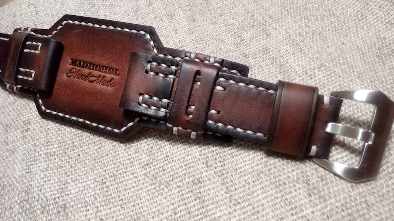 May include: Brown leather watch strap with white stitching and a silver buckle. The strap has the text "MADHOMOL Hand Made" embossed on it.
