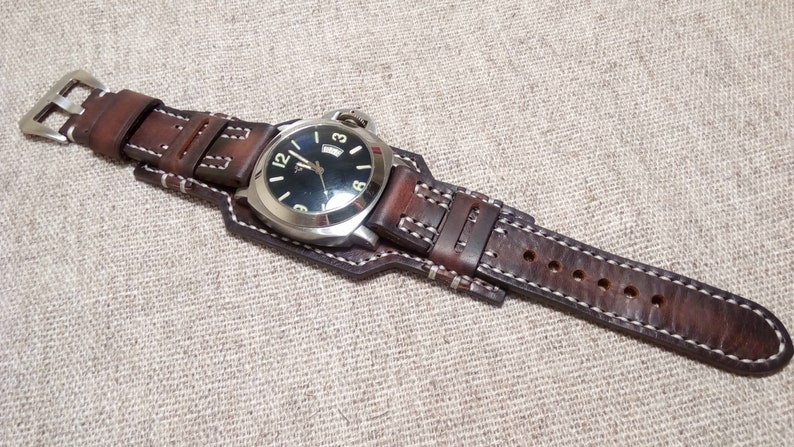 May include: A brown leather watch strap with white stitching. The strap is attached to a silver watch with a black face and white numbers.