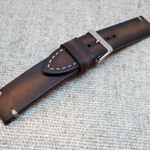 May include: A brown leather watch strap with white stitching and a silver buckle.