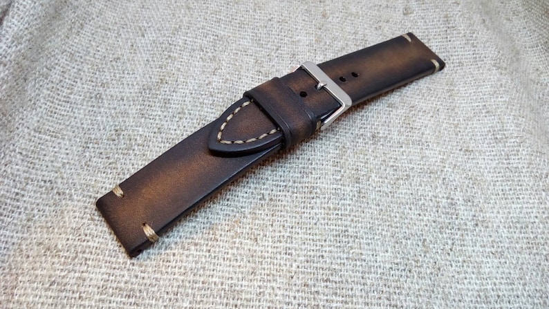 May include: A brown leather watch strap with white stitching and a silver buckle.