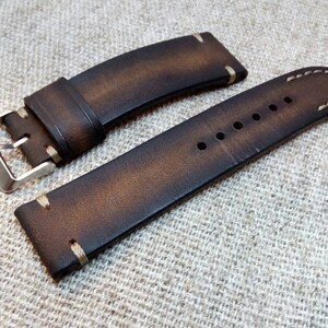 May include: A brown leather watch strap with white stitching. The strap has a silver buckle and is designed for a wristwatch.