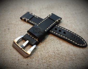 May include: Black leather watch strap with white stitching and a silver buckle. The strap has a logo with wings on it.