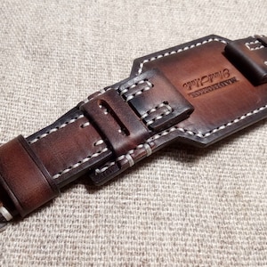 May include: A brown leather watch strap with white stitching and a silver buckle. The strap has a leather keeper with the text "TIP-TOP" embossed on it.
