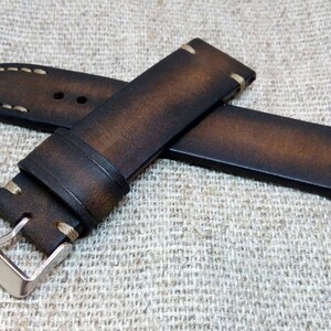 May include: A brown leather watch strap with white stitching and a silver buckle.