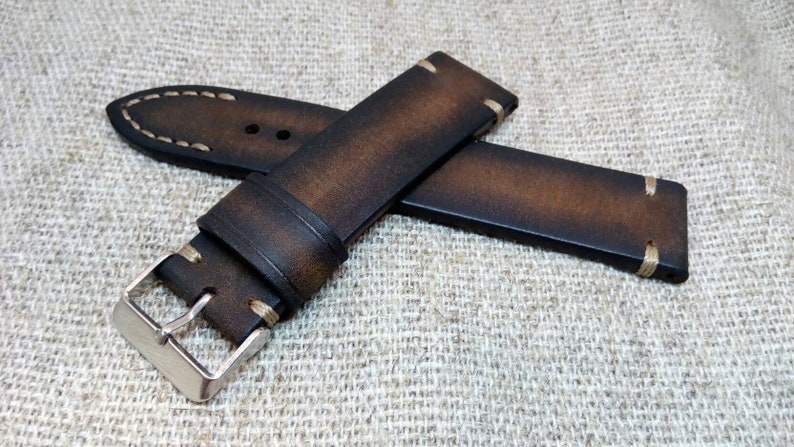 May include: A brown leather watch strap with white stitching and a silver buckle.