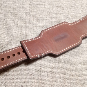 May include: Brown leather watch band with white stitching. The band has a buckle closure and is designed to fit a wrist.