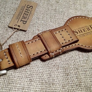 May include: A tan leather watch strap with a silver buckle. The strap has decorative stitching and the brand name "SHERP" is visible. A small tag with the brand name is attached.