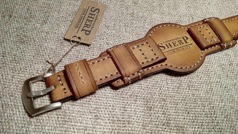 May include: A tan leather watch strap with a silver buckle. The strap has decorative stitching and the brand name "SHERP" is visible. A small tag with the brand name is attached.