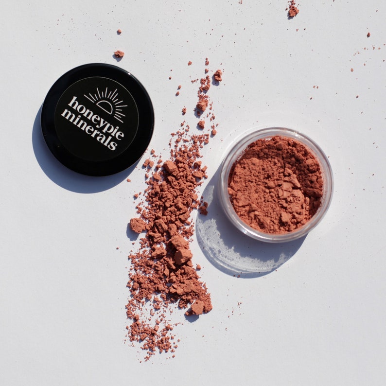 May include: A small, clear container of loose, reddish-brown powder with the label "honeypie minerals" on the lid.