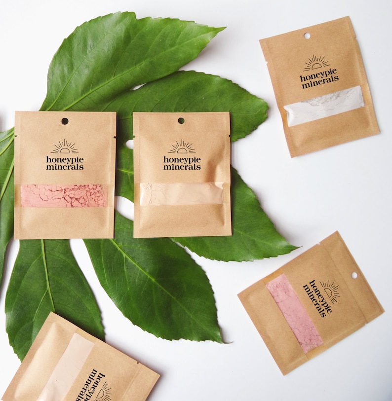 May include: Five small brown paper pouches with a sun and the text "honeypie minerals" on each. The pouches are arranged on a green leaf background.