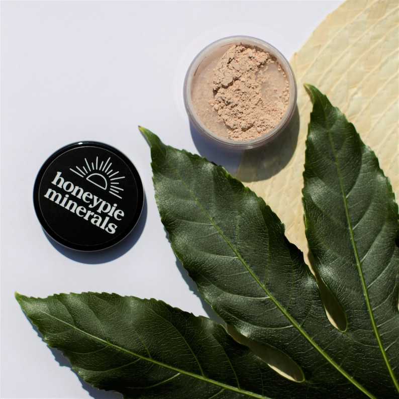 May include: A black container with the text "honeypie minerals" and a sun graphic. The container is open and shows a light beige powder inside.