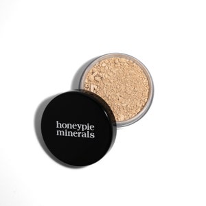 May include: A black container with the text "honeypie minerals" on the lid. The container is open and filled with a light brown mineral powder.