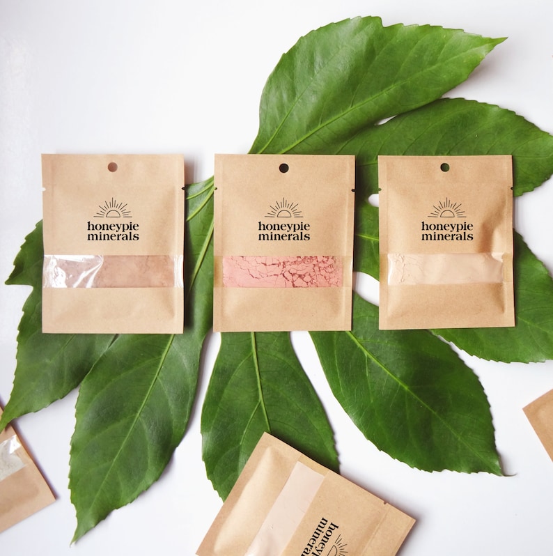 May include: Three small brown paper packets with a white sun and the text "honeypie minerals" printed on each. The packets contain different colored powders.
