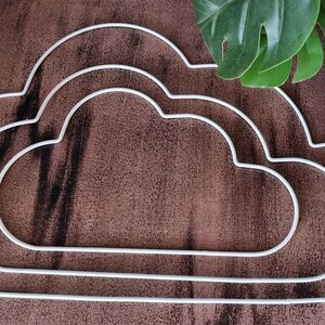 May include: Three white metal cloud-shaped hoops, nested together, on a brown wooden surface.