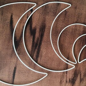 May include: Four white metal crescent moon shapes of varying sizes, arranged in a cascading pattern on a brown wooden surface.