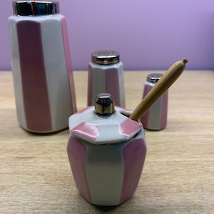 Peut inclure: Ensemble de quatre salières et poivrières en céramique rayées rose et blanc avec des dessus argentés. L'ensemble comprend un petit pot avec un couvercle et une cuillère en bois.