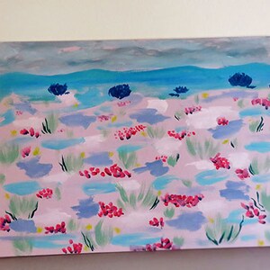 May include: A painting depicting a landscape with a pink background and blue and green brushstrokes. The painting features a blue sky with white clouds and a blue body of water in the distance. There are pink and red flowers scattered throughout the landscape.