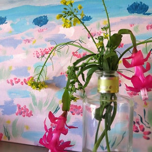 May include: A clear glass vase with a yellow lid holds a bouquet of pink and yellow flowers against a painted background of pink, blue, and green.
