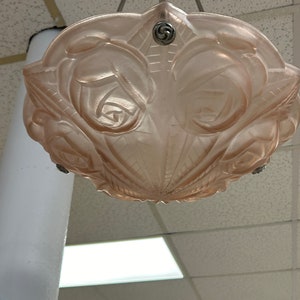 Pode incluir: Um candeeiro de teto de vidro rosa com um design de rosas. O candeeiro est&aacute; pendurado numa corrente.