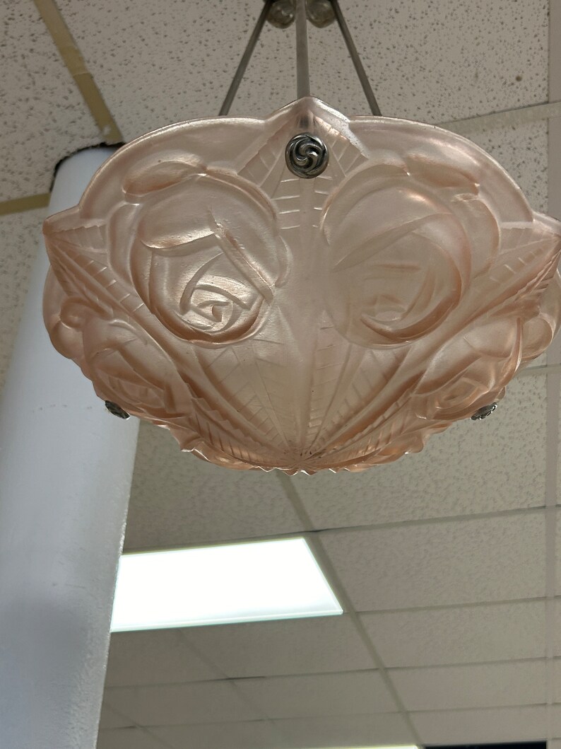 Pode incluir: Um candeeiro de teto de vidro rosa com um design de rosas. O candeeiro est&aacute; pendurado numa corrente.
