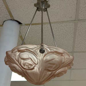 Pode incluir: Um candeeiro de teto de vidro rosa com um design floral. O candeeiro est&aacute; suspenso do teto por tr&ecirc;s correntes met&aacute;licas.