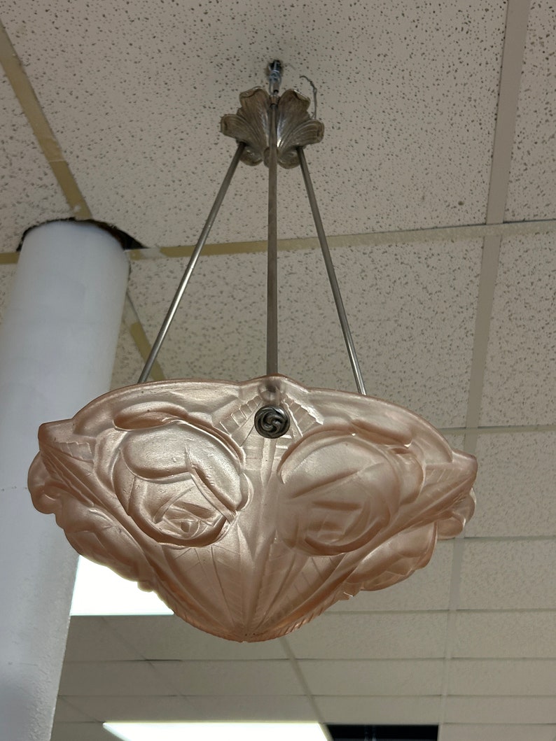 Pode incluir: Um candeeiro de teto de vidro rosa com um design floral. O candeeiro est&aacute; suspenso do teto por tr&ecirc;s correntes met&aacute;licas.