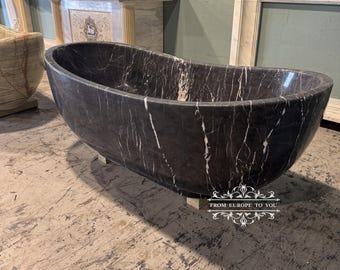 May include: A black and white marble bathtub with a smooth, polished finish. The bathtub is freestanding and has a classic oval shape. The bathtub is sitting on a light brown floor.