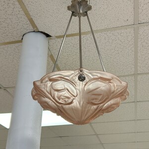 Pode incluir: Um pendente de luz de vidro rosa com um design floral pendurado em uma corrente prateada.