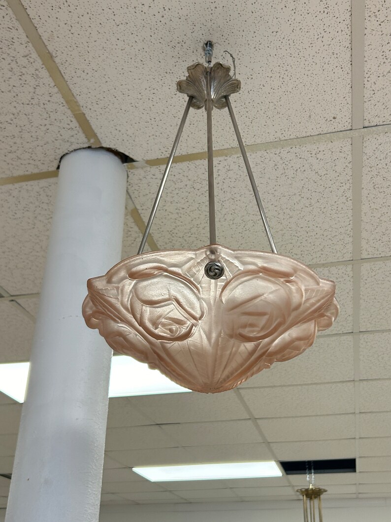 Pode incluir: Um pendente de luz de vidro rosa com um design floral pendurado em uma corrente prateada.
