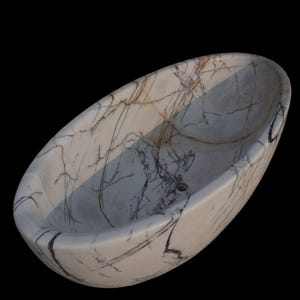 May include: Oval-shaped marble sink with a white base and intricate gray and brown veining. The sink has a smooth, polished surface and a drain hole. The design is a natural stone pattern, suitable for a bathroom.