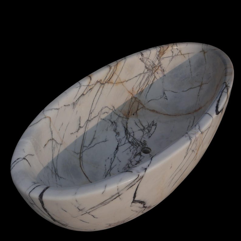 May include: Oval-shaped marble sink with a white base and intricate gray and brown veining. The sink has a smooth, polished surface and a drain hole. The design is a natural stone pattern, suitable for a bathroom.