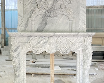 May include: A white marble fireplace mantel with intricate carvings of flowers and leaves. The mantel has a large, ornate design and is made of high-quality marble.