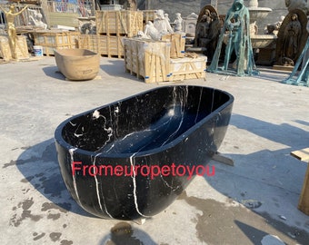 May include: A black and white marble bathtub with a rounded oval shape. The bathtub is sitting on a concrete surface.