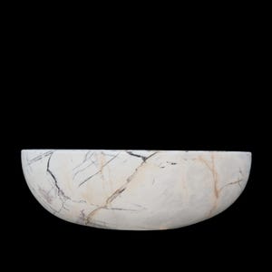 May include: A white marble bowl with a semi-circular shape. The bowl has dark gray and brown veining throughout the surface. The background is solid black.