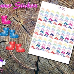 May include: Planner stickers featuring colorful rain boots in various shades, including pink, blue, and red, with white polka dots. A sheet of stickers displays multiple pairs of boots in pastel colors. The background is a wooden surface.