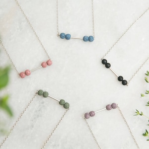 Puede incluir: Cinco collares de plata con una barra y tres cuentas de roca volcánica. Las cuentas son de diferentes colores: azul, negro, verde, rosa y morado.