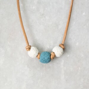 Könnte beinhalten: Eine braune Lederkordelkette mit drei Perlen. Die Perlen sind weiß und blau. Die blaue Perle befindet sich in der Mitte.