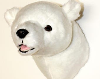 May include: A plush polar bear head wall mount featuring soft white fur, rounded ears, dark brown eyes, a black plastic nose, and an open mouth revealing a pink tongue and small white teeth, designed to be displayed as a decorative wall accent.