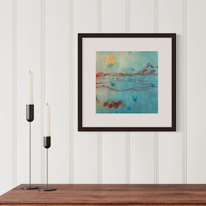 May include: A framed abstract watercolor painting with a blue and green background, a red and orange sun, and red and orange mountains in the distance. There are also red and orange circles in the bottom right corner of the painting.