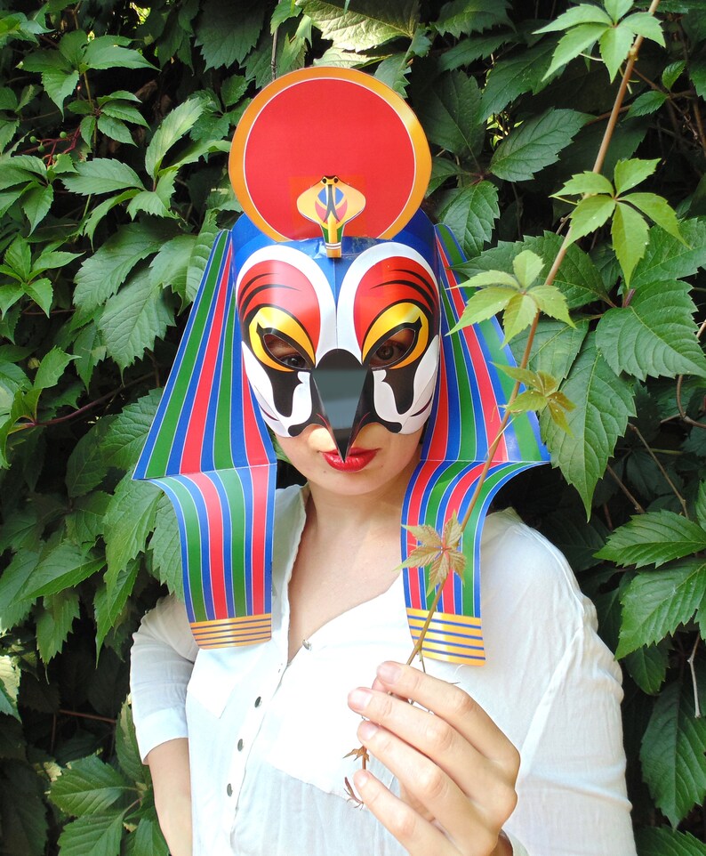 May include: A colorful paper mask with a red, white, and blue striped design. The mask features a bird-like face with a black beak and a red crown.