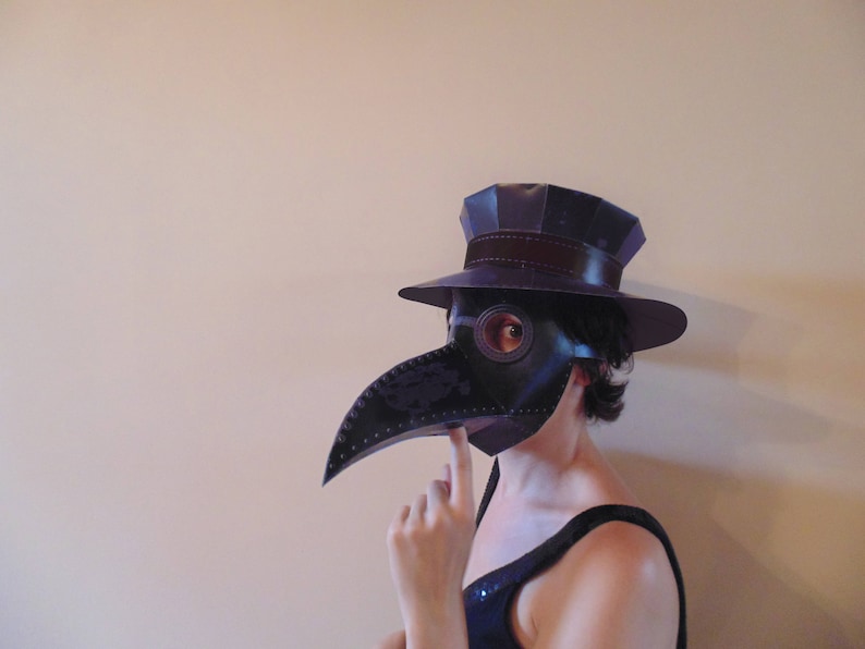 May include: A person wearing a black and purple plague doctor mask with a black hat and a black and white patterned dress.