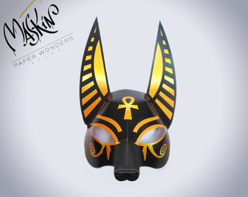 May include: Black and gold papercraft mask with an Ankh symbol on the forehead and stylized eyes. The mask has large, pointed ears with gold and black stripes.
