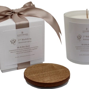 Op de afbeelding: Een witte kaars met een houten deksel in een witte doos met een bruin lint. De kaars en de doos hebben een label met de tekst "2nd Wedding Anniversary" en "Mr & Mrs Kent".