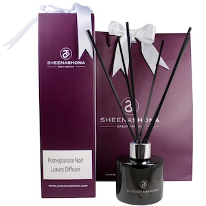 Op de afbeelding: Een zwarte glazen diffuserfles met een zilveren dop en zwarte rietjes. De fles is gelabeld met "Pomegranate Noir Luxury Diffuser" en "Sheenashona Great Britain".