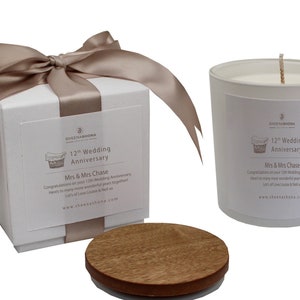 Op de afbeelding: Een witte kaars met een houten deksel in een witte doos met een bruin lint. De kaars en de doos hebben een label met de tekst "12e huwelijksverjaardag" en "Mevrouw en Mevrouw Chase".