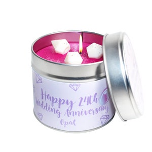 May include: A silver tin candle with a pink wax base and white diamond-shaped decorations. The label reads "Happy 24th Wedding Anniversary Opal".