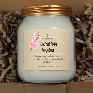 May include: A white jar candle with a gold lid and a label that reads "Gone But Never Forgotten." The label also includes a pink floral design and the text "I miss you each and every year but hold you so dear in my heart David, Love Mum xx www.sheenashona.com".