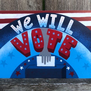 May include: A blue and red illustration with white stars, depicting a hand placing a ballot into a ballot box. The text "We Will Vote" is written in large, bold letters.