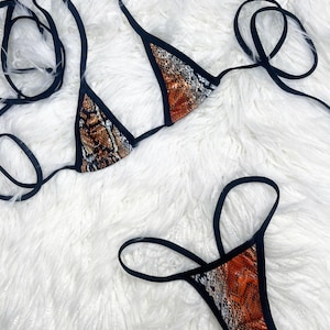 May include: A two-piece bikini set featuring a snakeskin print in shades of brown, orange, and white. The bikini top is a triangle style with black straps, and the bottom is a thong style with matching print and black trim.