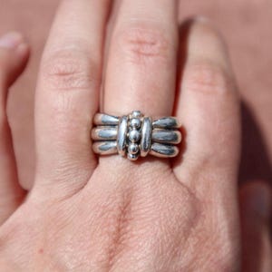 Peut inclure: Une bague en argent au design unique. La bague présente trois bandes superposées avec un groupe central de petites perles rondes. La bague est portée au doigt, mettant en valeur ses détails complexes et sa finition polie.